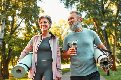 Two adults walking outdoors carrying exercise mats and a water bottle