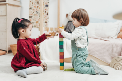 Two young children playing together and stacking colourful wooden blocks