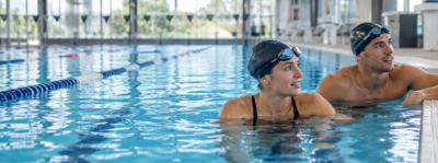 Two swimmers resting at the end of indoor pool lanes during training
